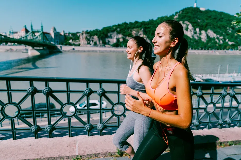 Two smiling women jogging together along a riverside path