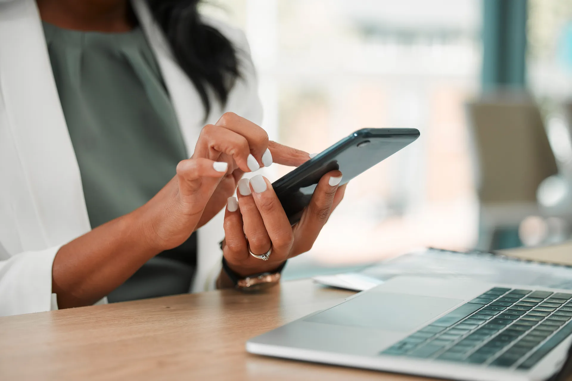 Woman at a desk using a smartphone next to an open laptop