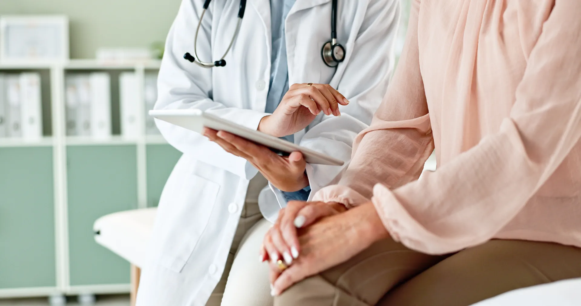 Doctor with a stethoscope shows a tablet to a seated patient during a consultation