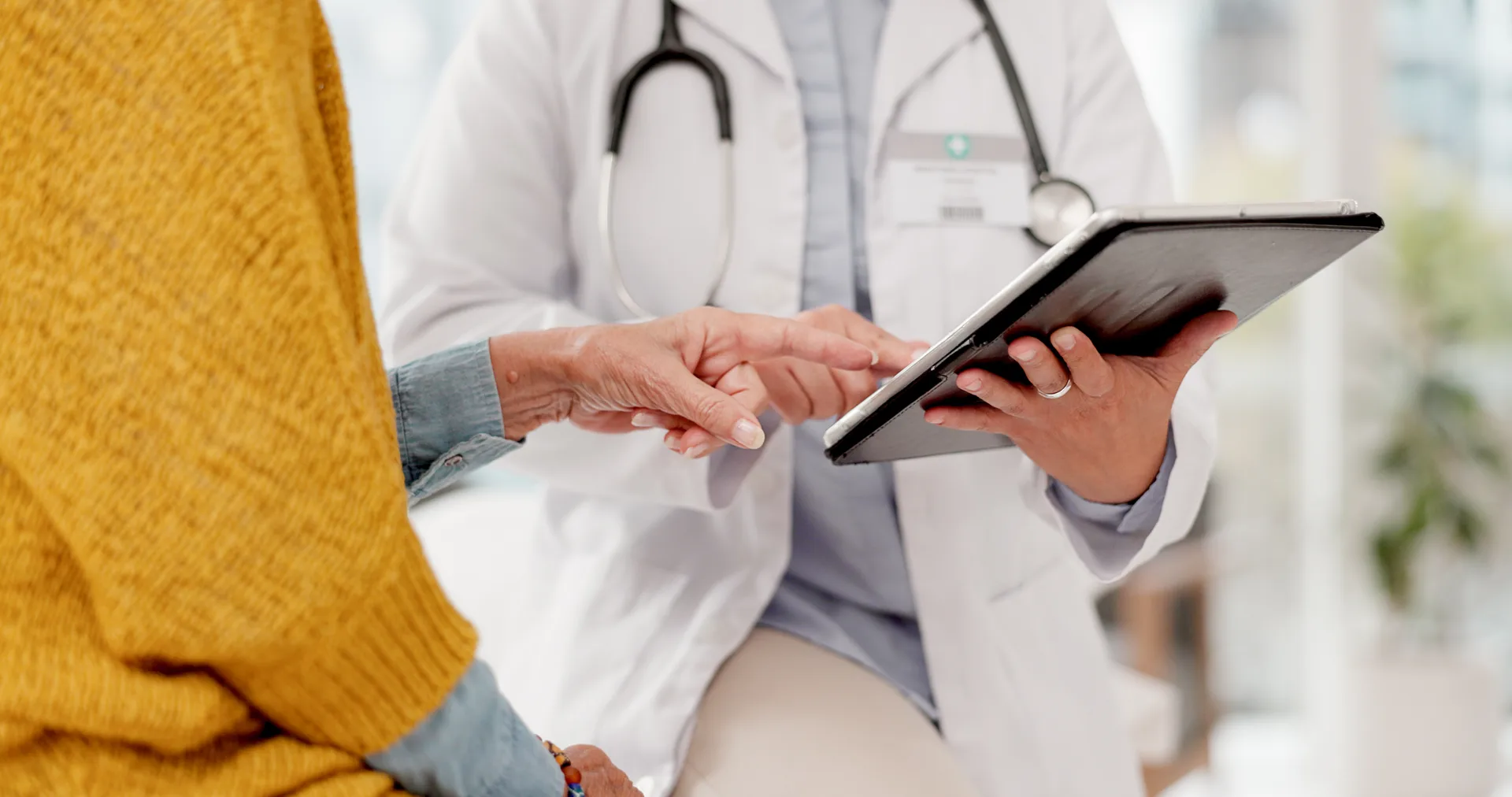 Doctor in a white coat showing a tablet to a patient who points at the screen
