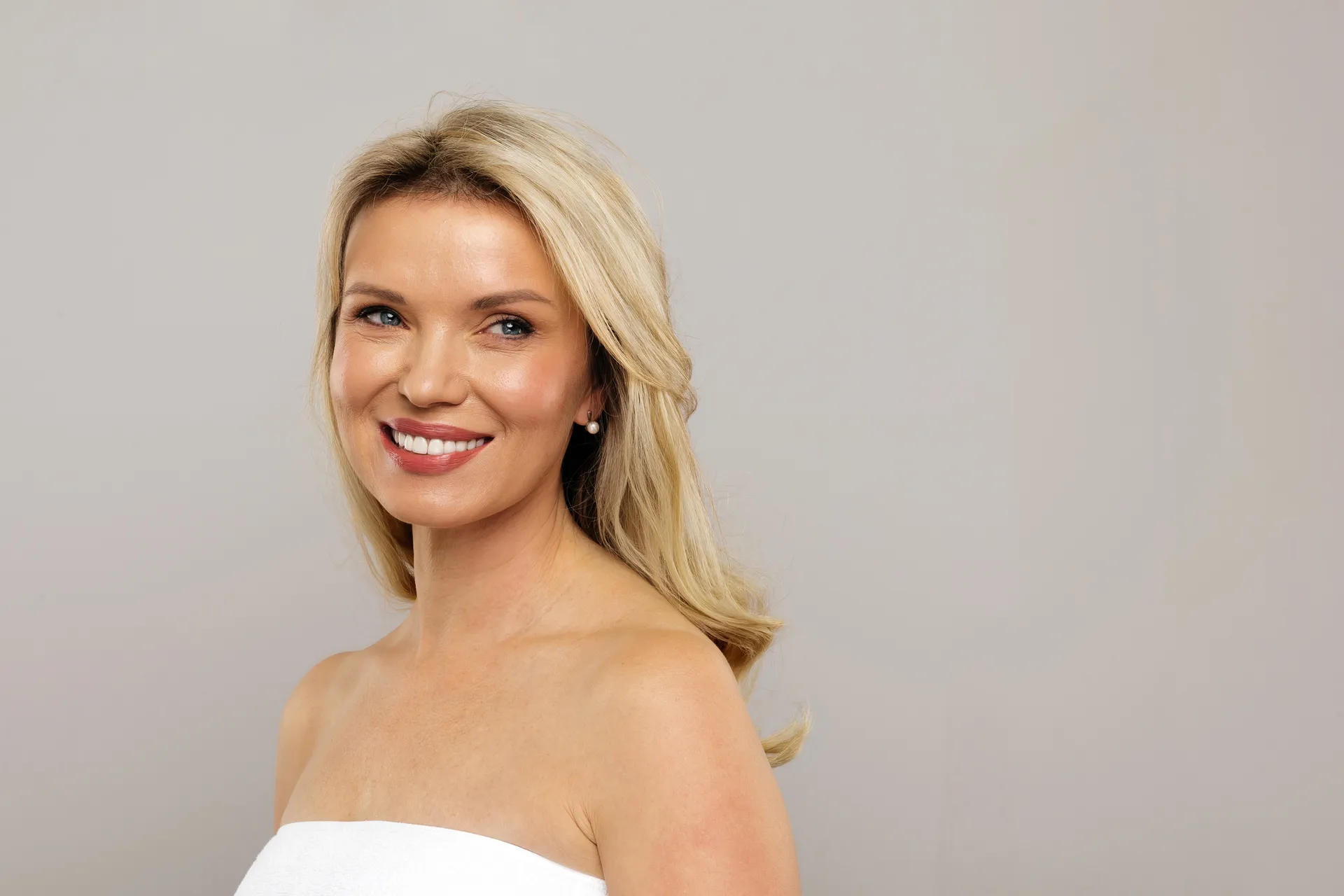 Smiling blonde woman with glowing skin posing against a plain gray background