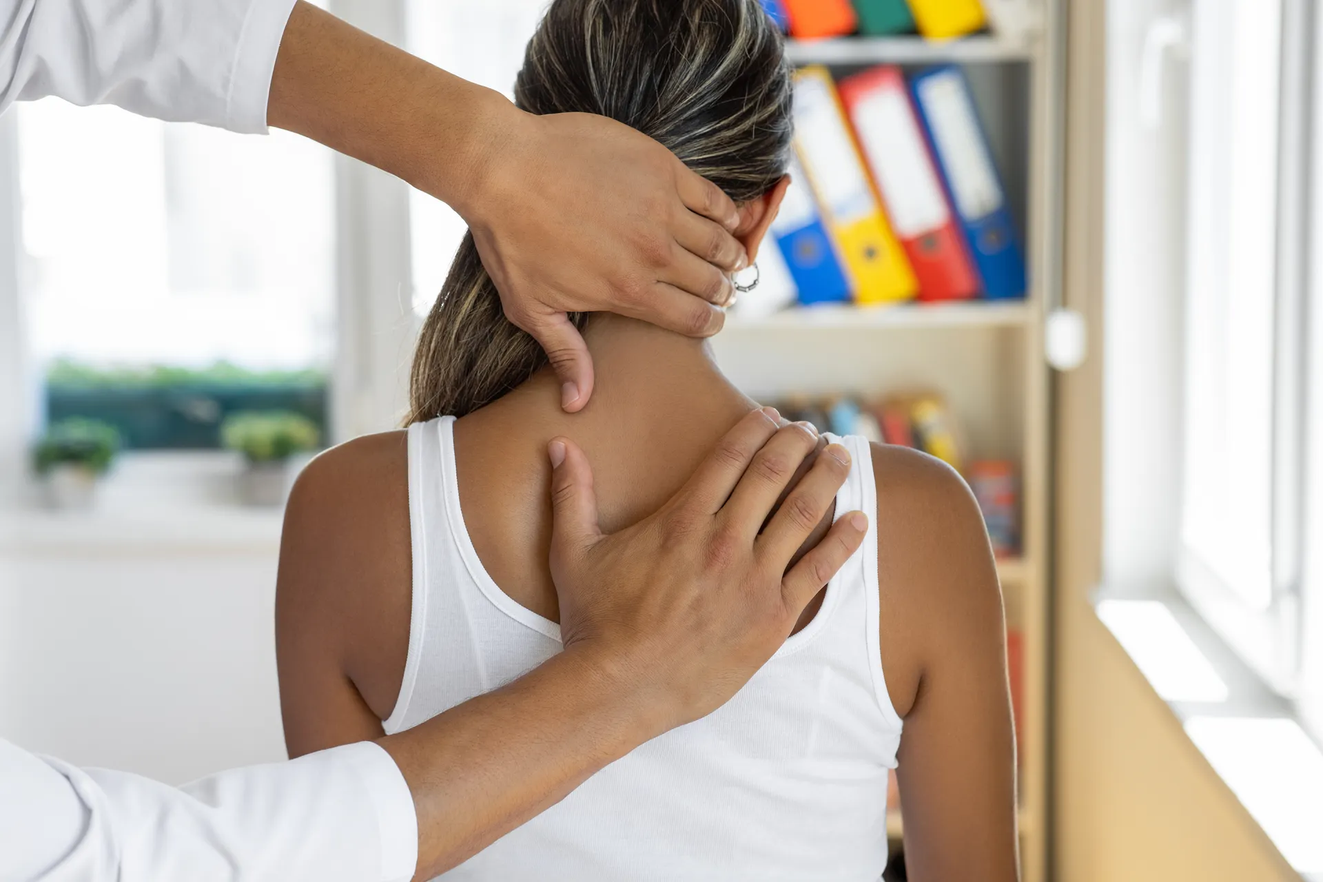Practitioner's hands examining a woman's neck and upper back