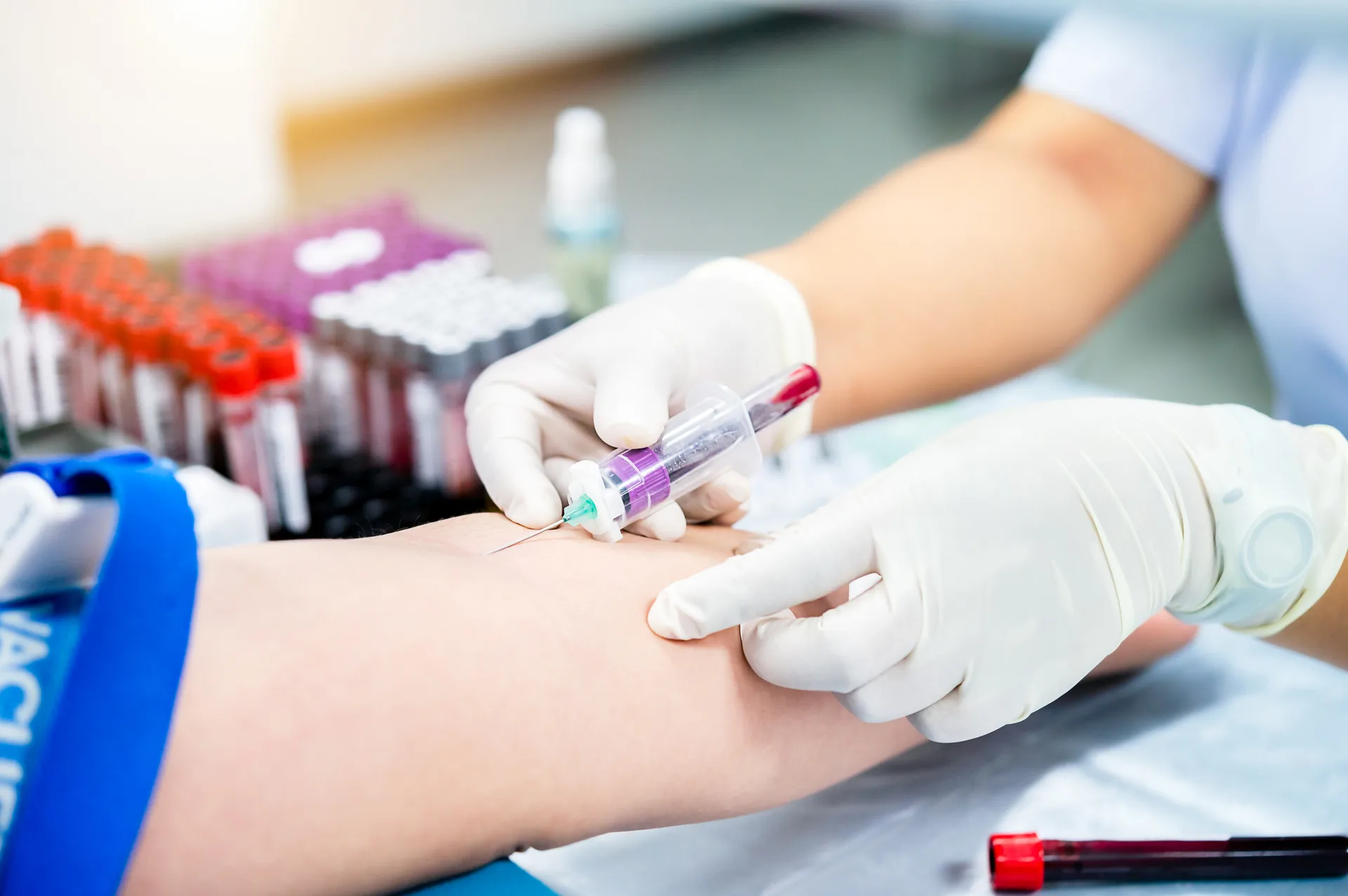 Gloved hands drawing blood from a patient's arm with sample tubes nearby