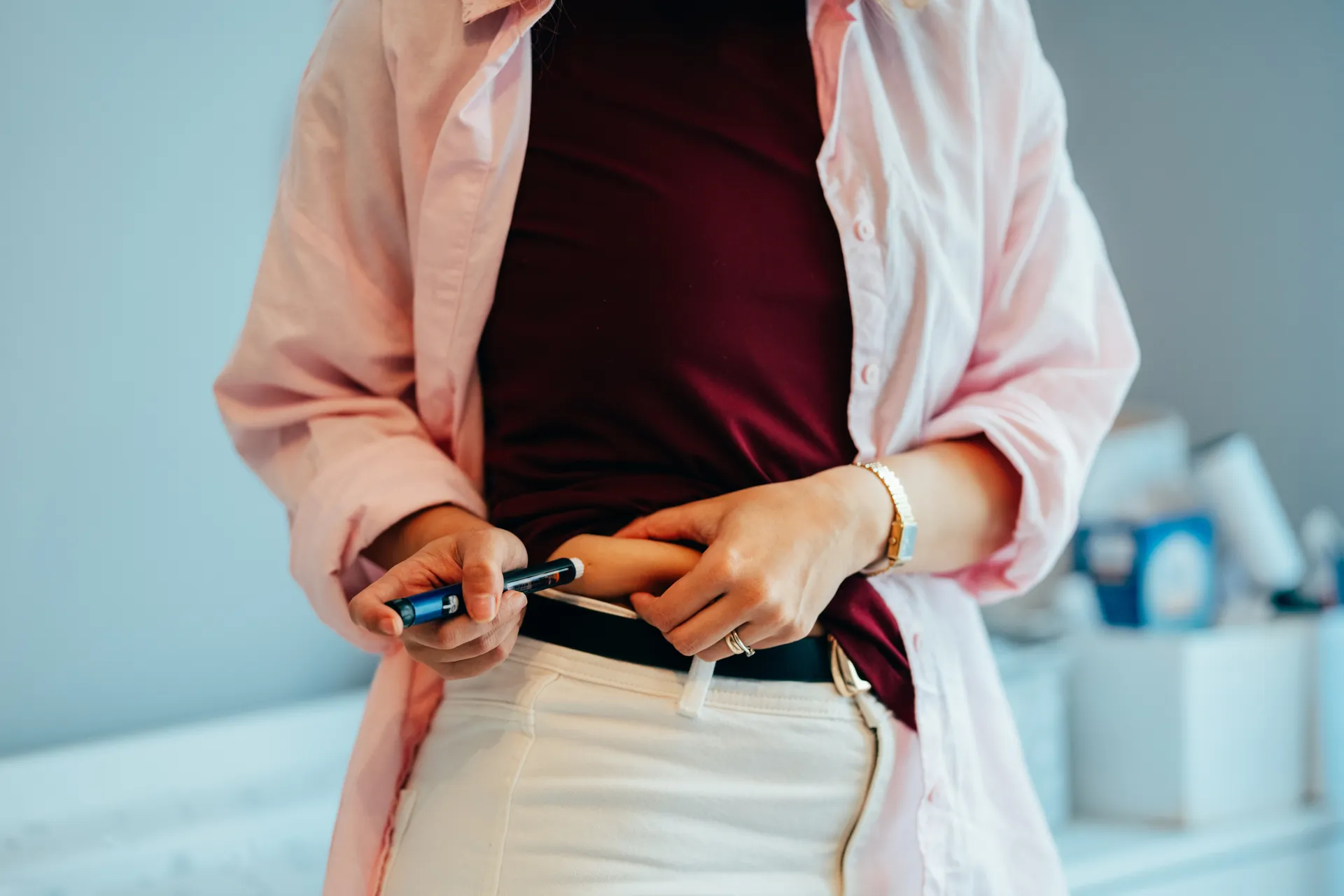 Woman holding an injection pen to her abdomen while lifting her top