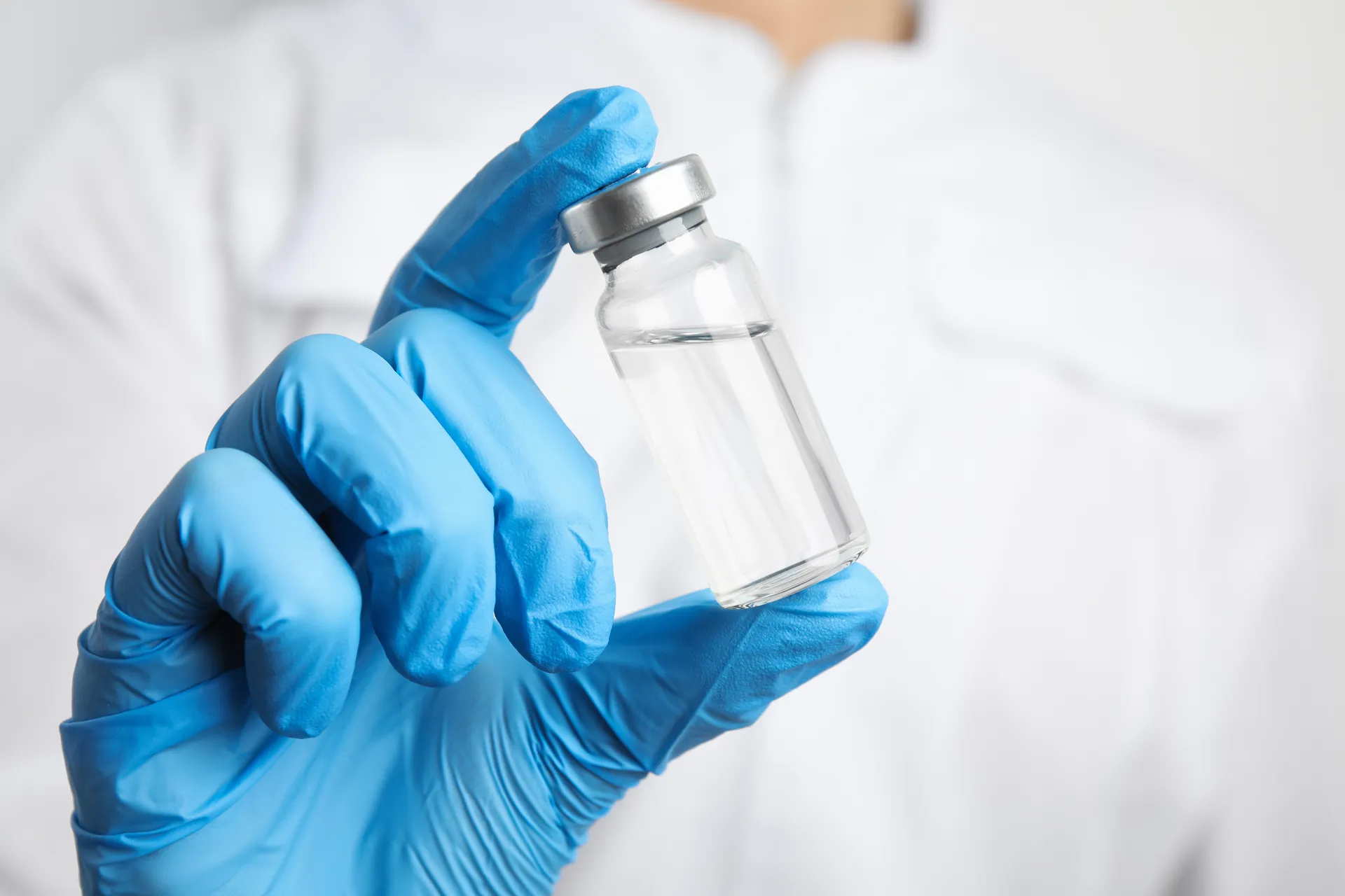 Gloved hand holding a small glass vial of clear liquid