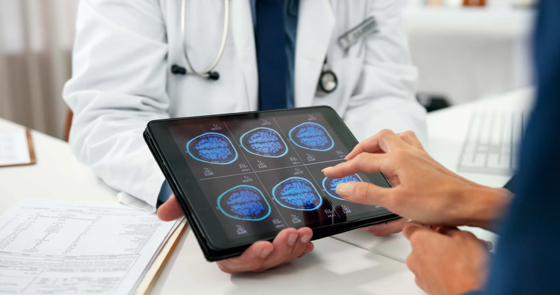 Doctor holds a tablet displaying brain scans while a patient points to one of the images