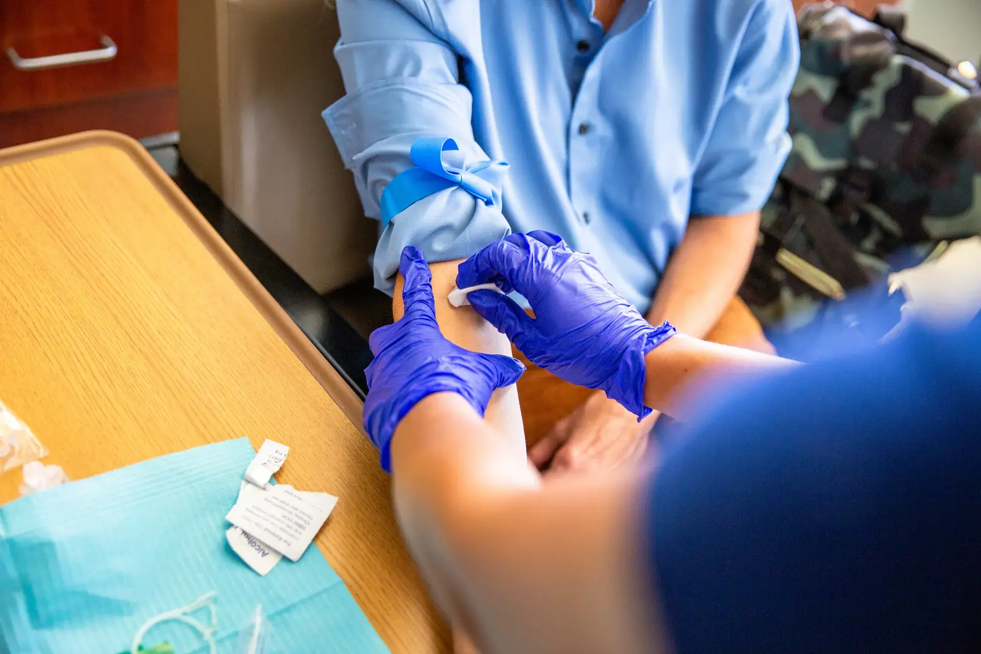 Clinician in purple gloves preparing a man's arm for a blood draw below a blue tourniquet