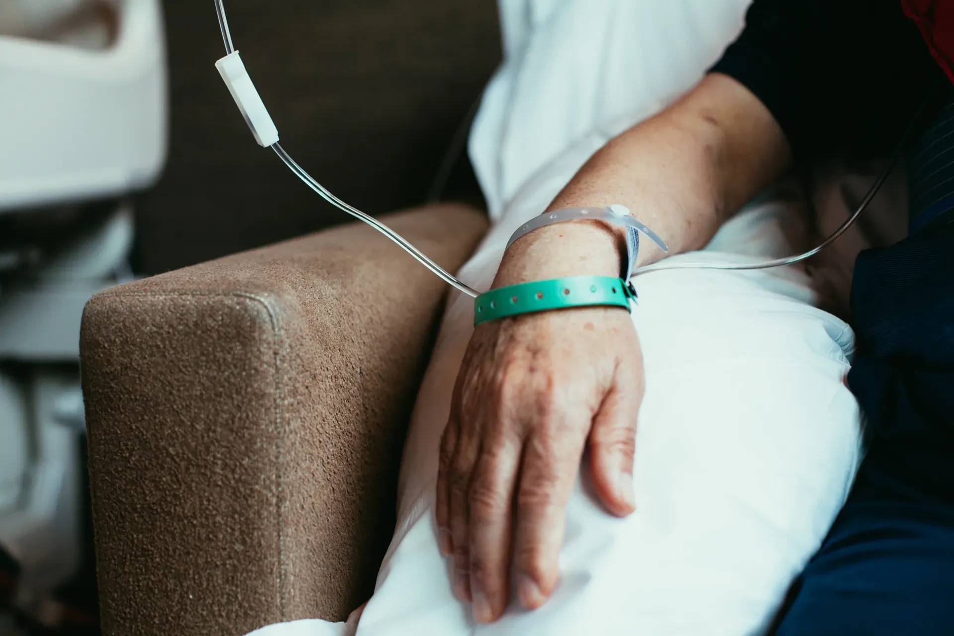 Older patient's hand resting on a pillow with an IV line and a green wristband