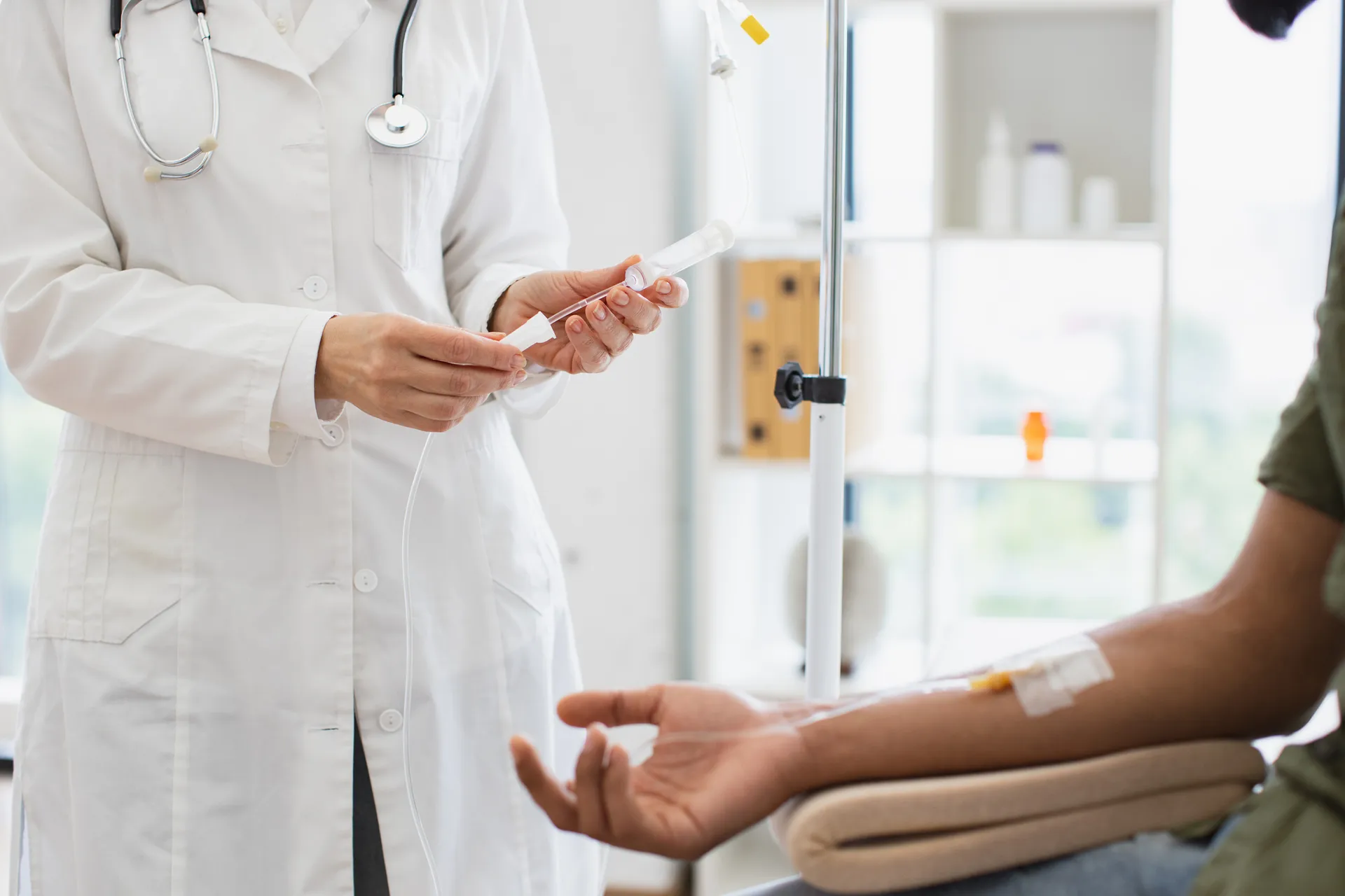 Doctor preparing IV tubing beside a seated patient with a catheter taped to the arm