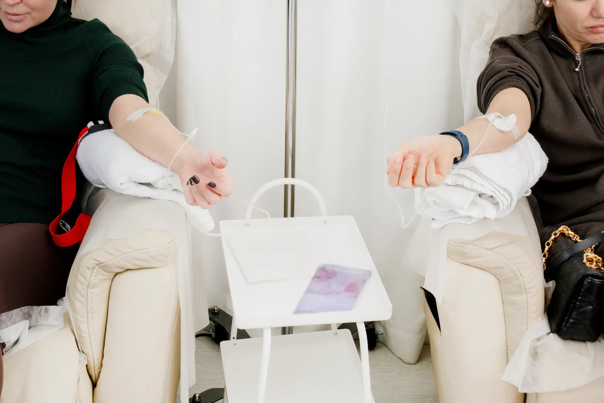Two women seated in recliners receiving IV infusions with a small table between them