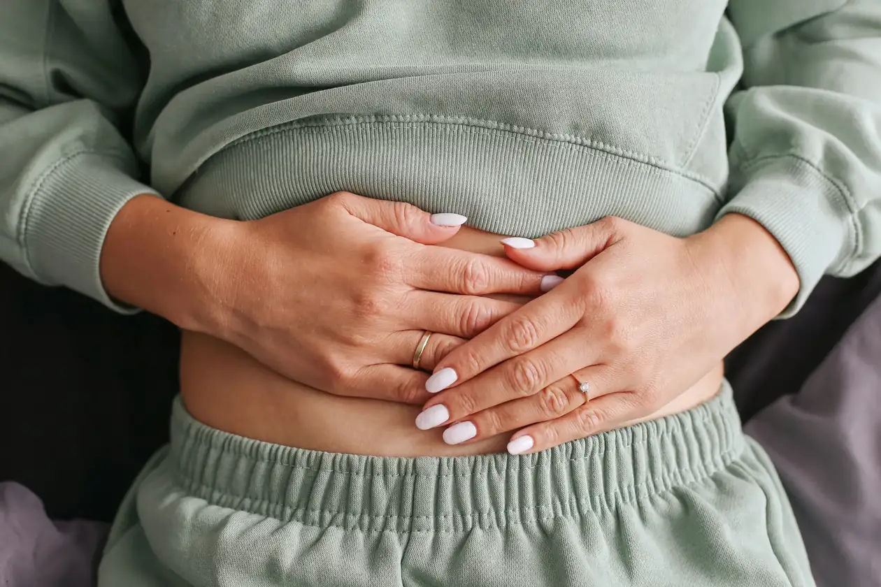 Person in a green sweatsuit resting both hands over their stomach