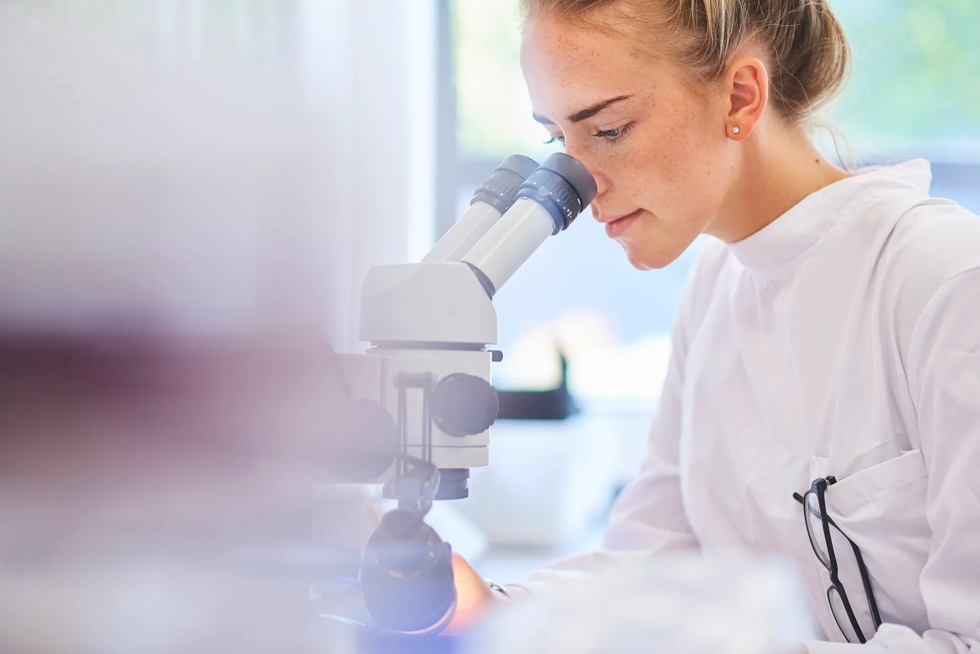 Lab worker in a white coat looks into a microscope