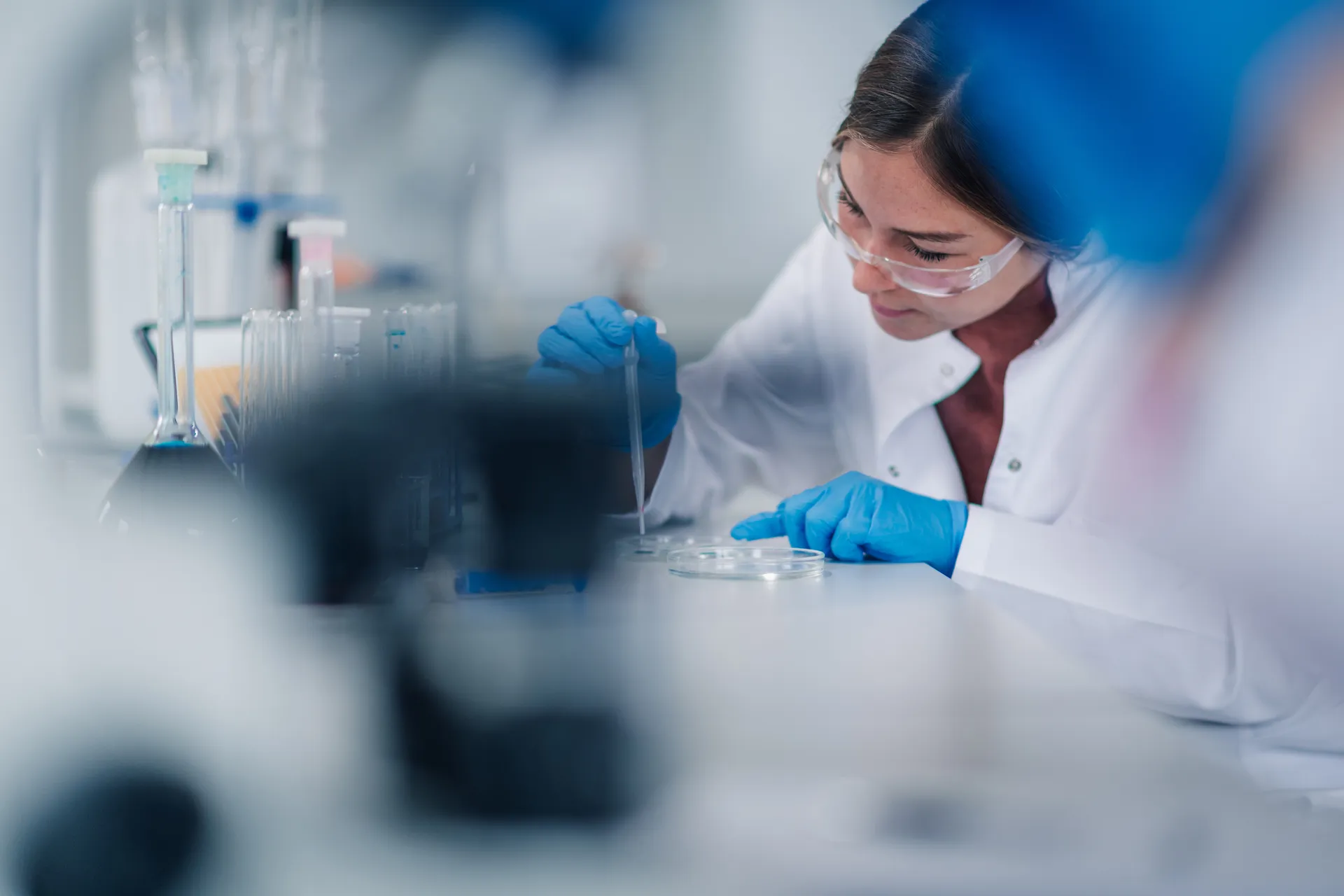 Lab scientist in safety glasses using a pipette over a petri dish