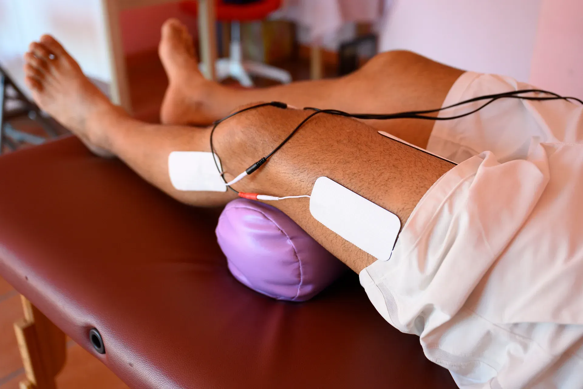 Electrode pads wired to a patient's lower leg resting on a treatment table