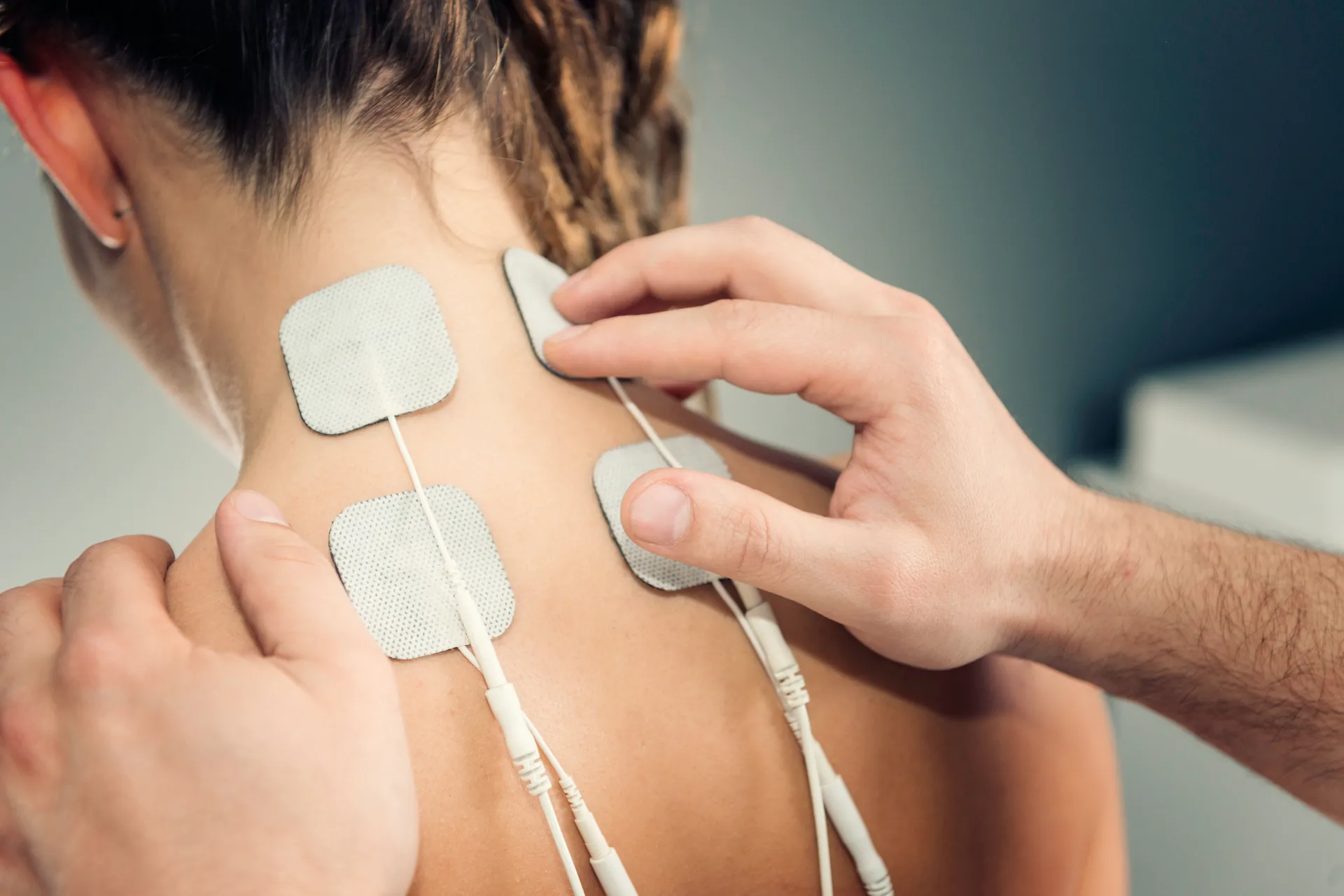 Therapist places electrode pads on the back of a woman's neck and upper shoulders