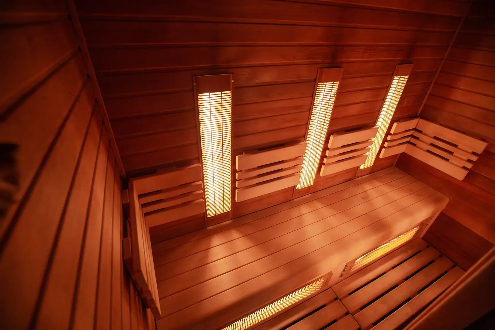 Empty wooden sauna cabin with glowing infrared heater panels on the walls and under the bench