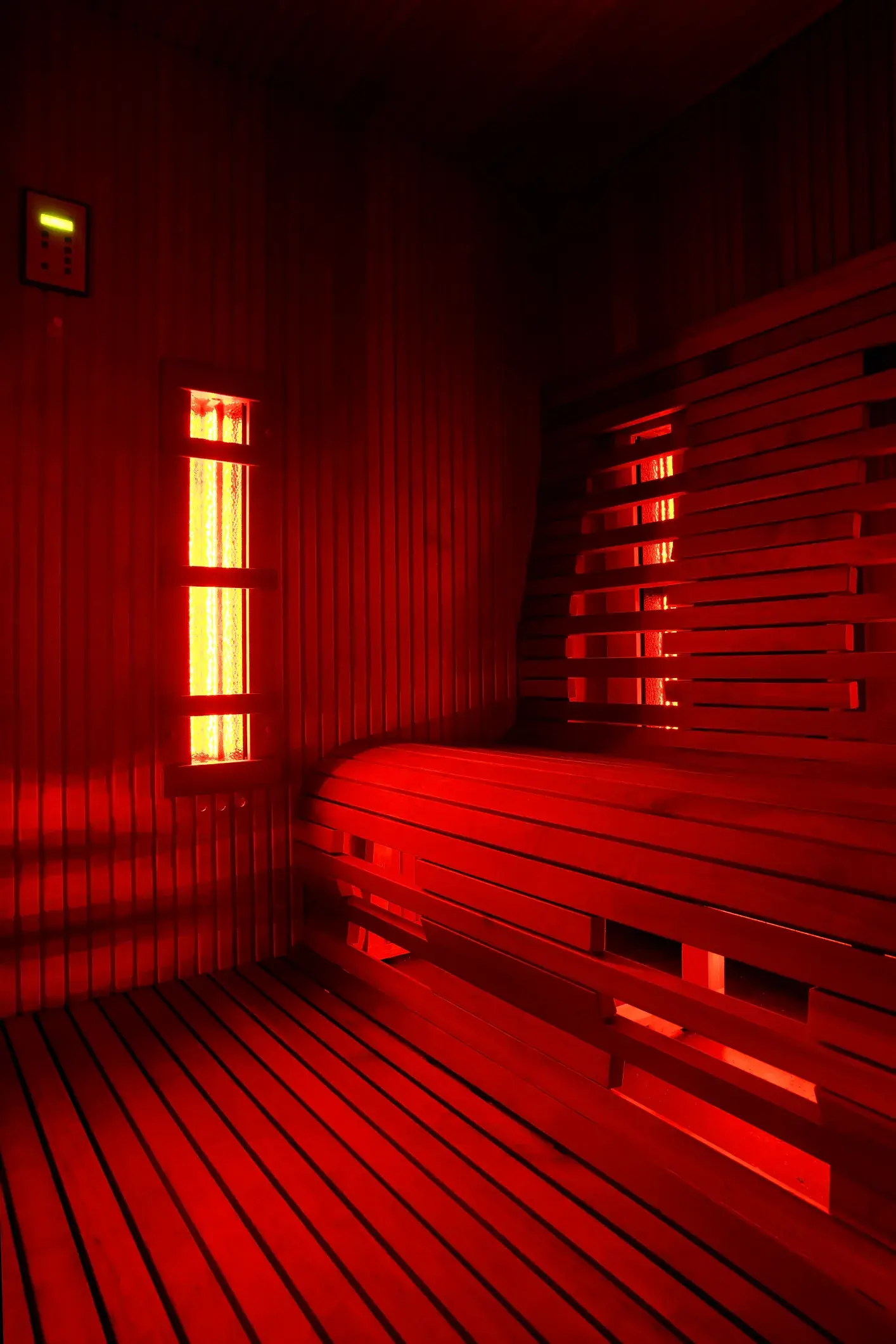 Empty wooden infrared sauna cabin with benches glowing under red heater light