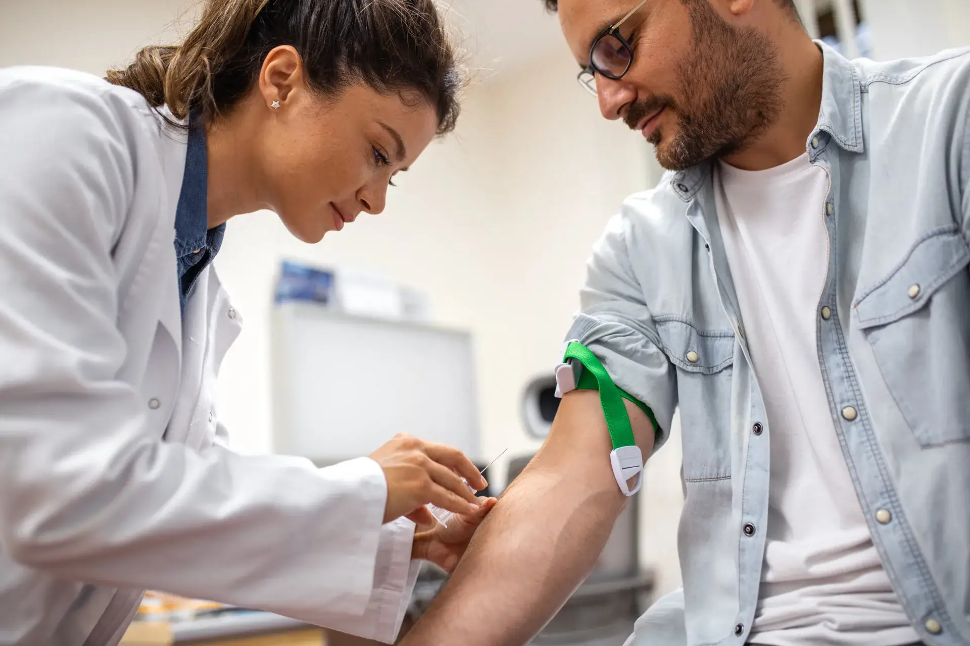 Clinician draws blood from a smiling man's arm with a green tourniquet above the elbow