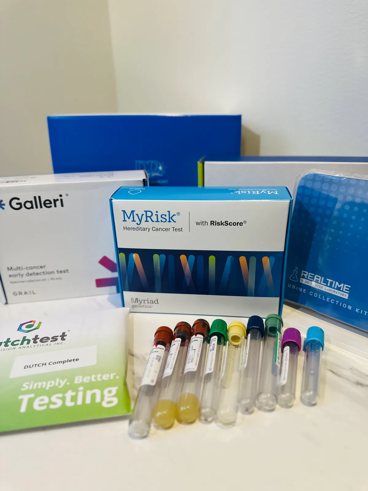Lab test kits including Galleri, MyRisk and DUTCH Complete boxes beside a row of capped blood collection tubes