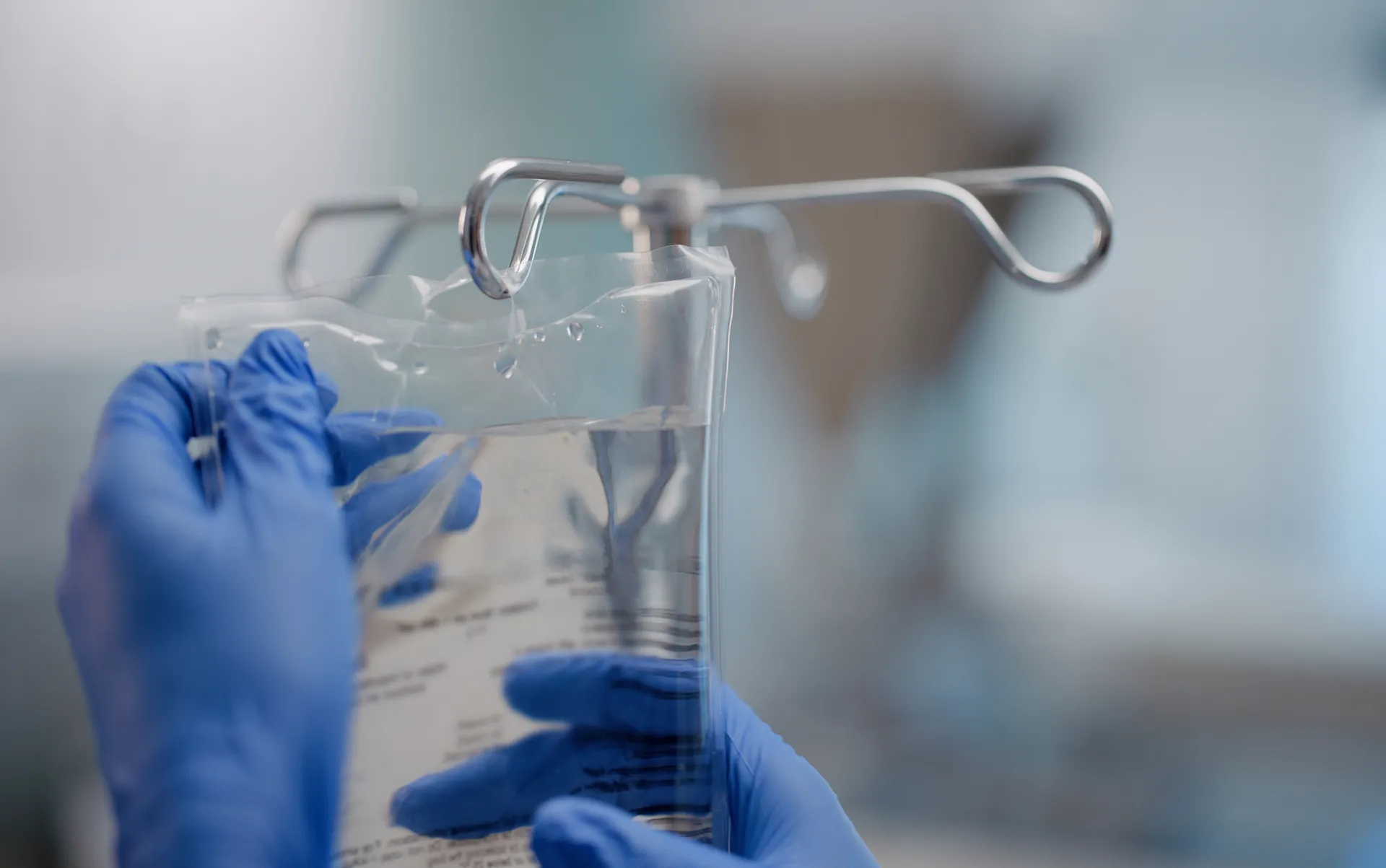 Gloved hands hanging a clear IV fluid bag on a metal stand