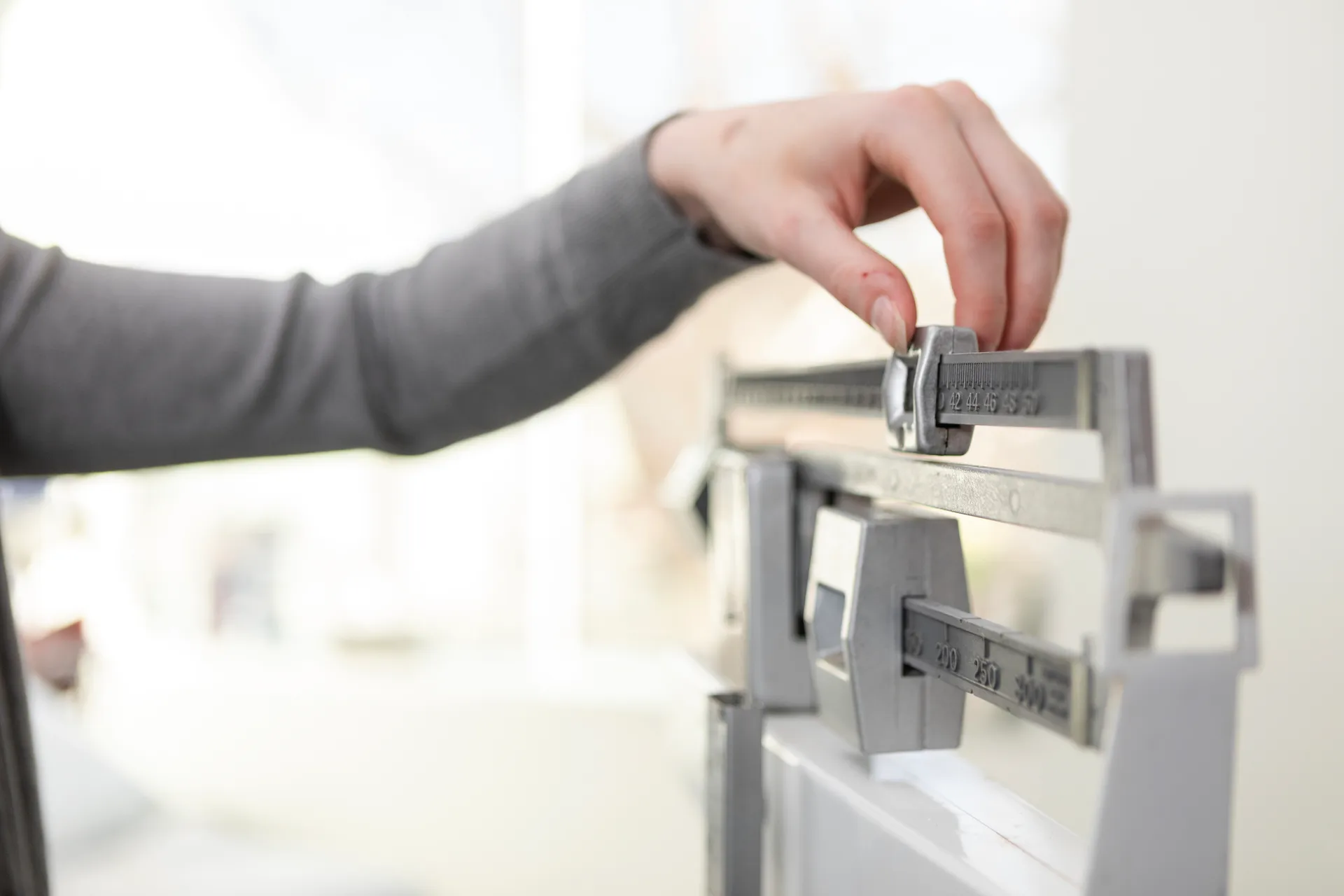 Hand adjusting the sliding weight on a medical balance beam scale