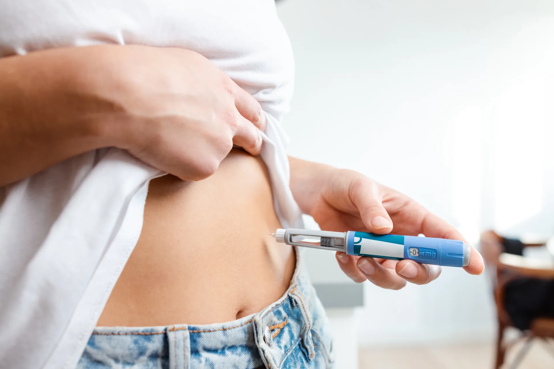 Person lifting a white shirt to inject the abdomen with a blue injection pen