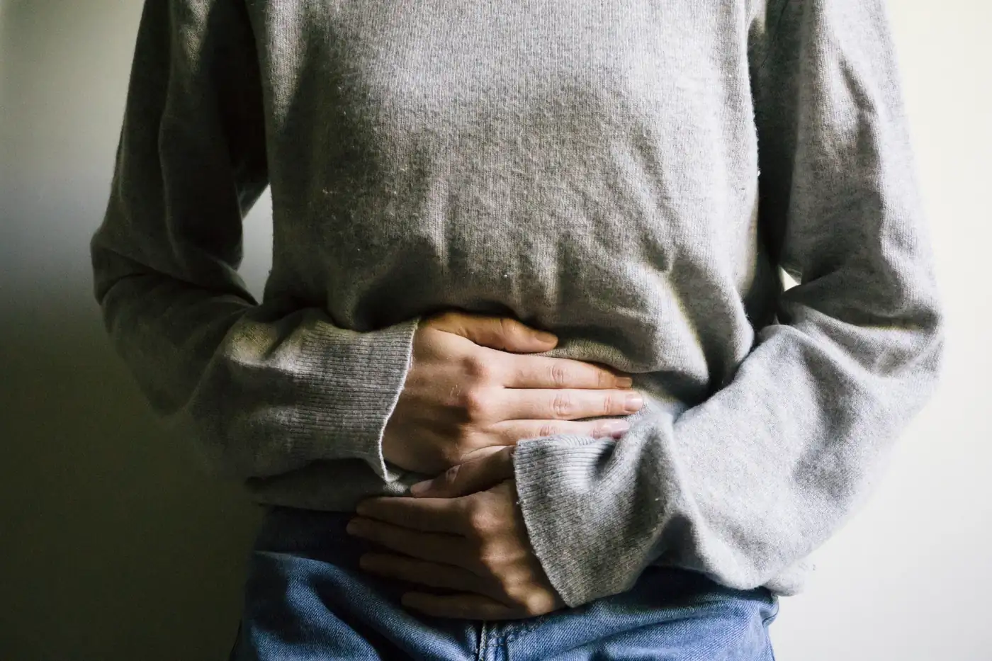 Person in a gray sweater holding both hands against their stomach