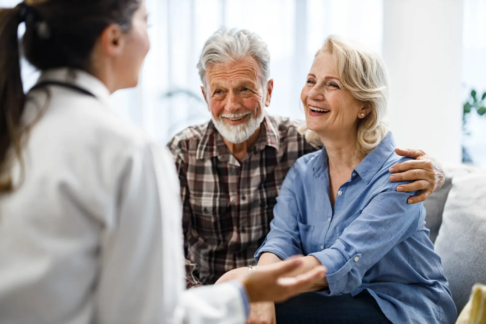 Smiling older couple sitting together on a sofa talking with a doctor
