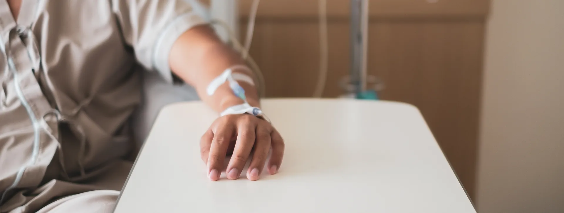 Patient's hand resting on a bedside table with an IV line taped to the back of the hand
