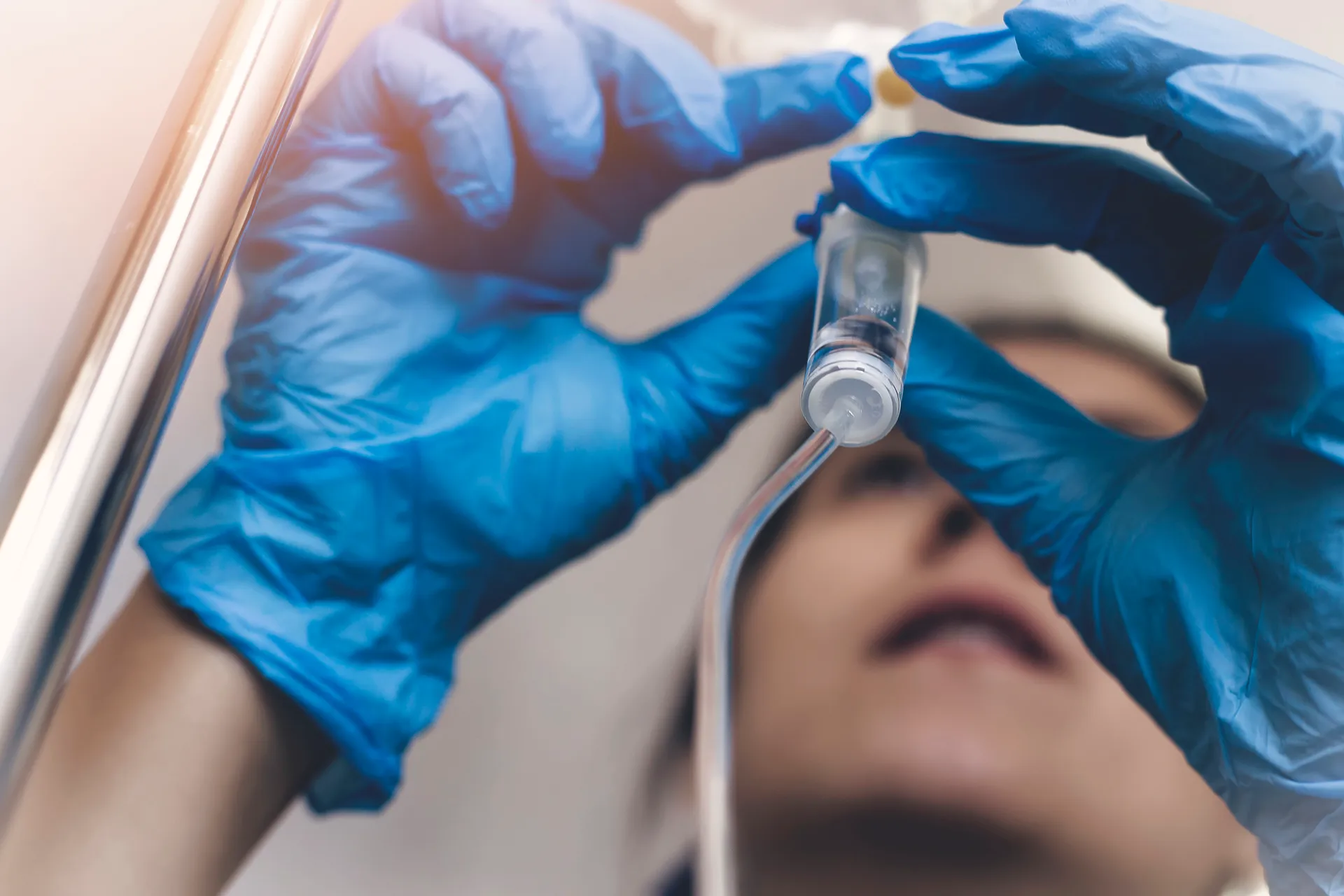 Gloved hands adjusting an IV drip chamber above a patient