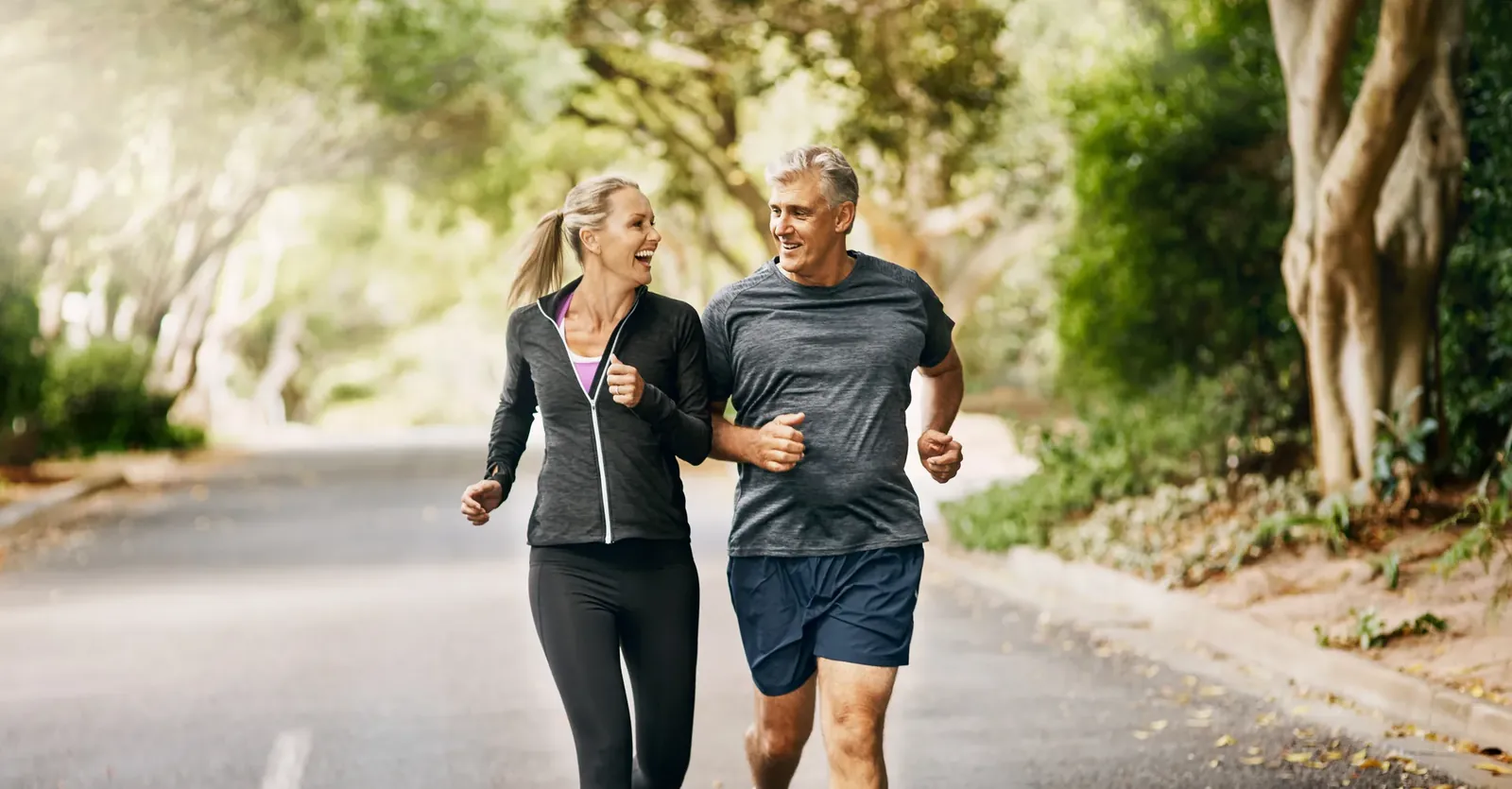 Smiling middle-aged couple jogging together on a tree-lined road