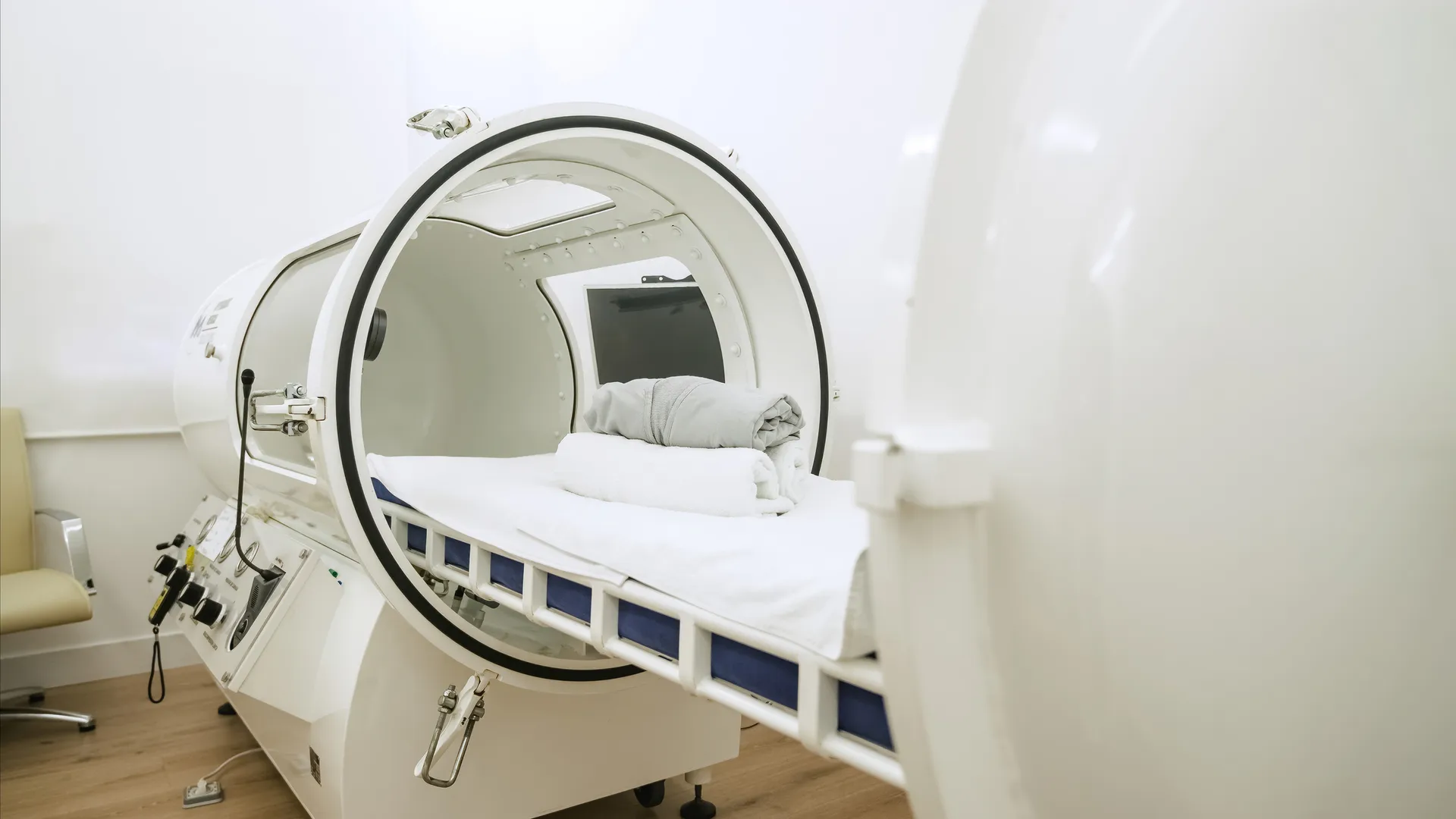 Open hyperbaric oxygen chamber with a padded bed, towel, and blanket inside