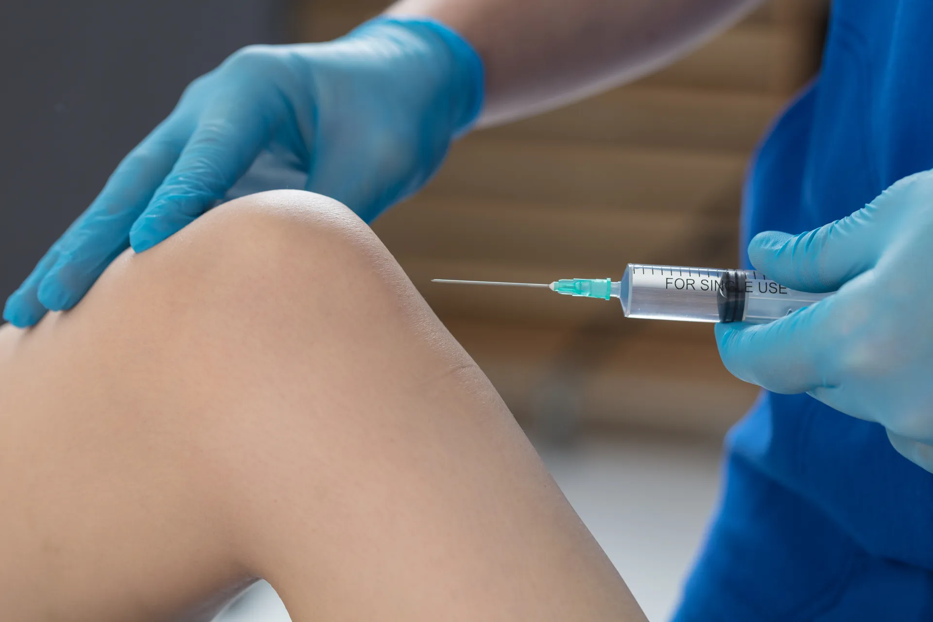 Gloved clinician steadies a patient's knee while holding a syringe ready for an injection