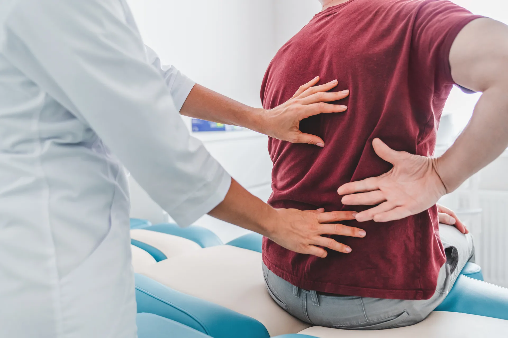 Clinician places her hands on a seated man's lower back as he holds his side in pain