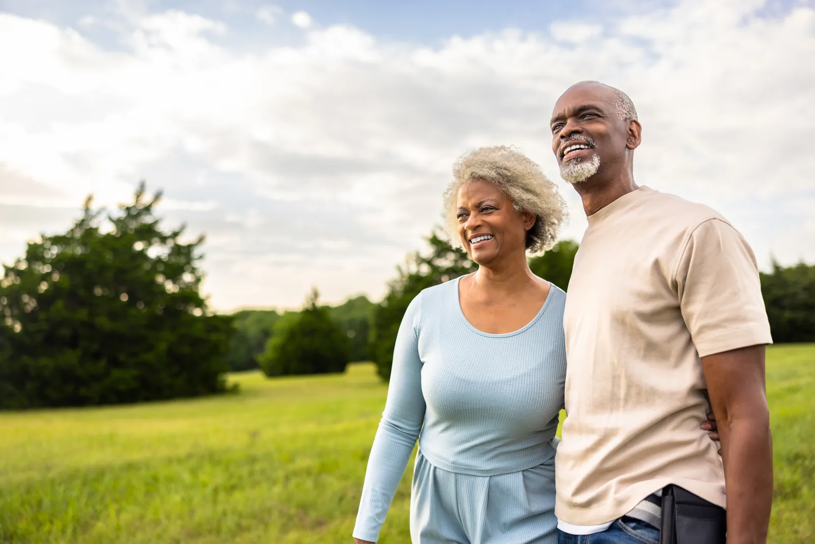 Smiling older couple standing arm in arm in a grassy field on a cloudy day