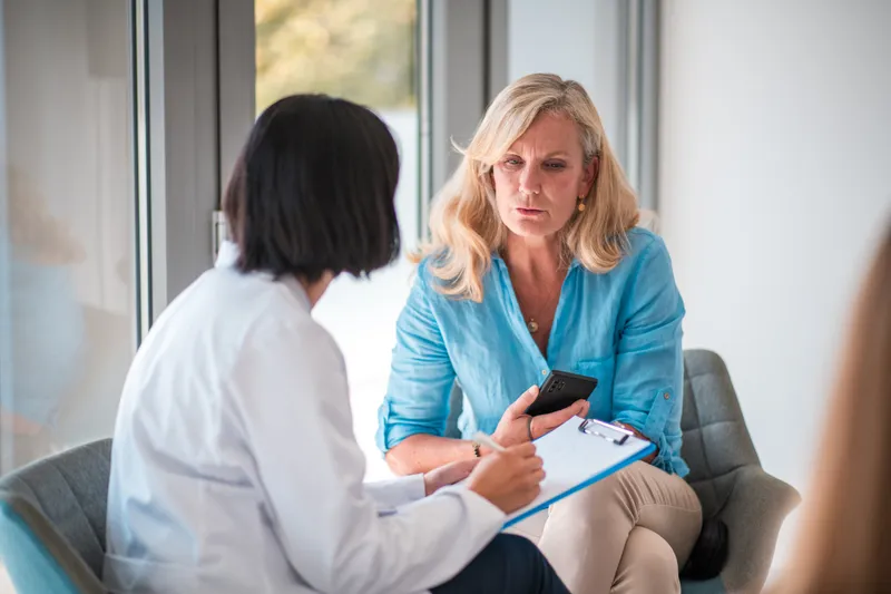 Woman in a blue shirt talks with a clinician who takes notes on a clipboard