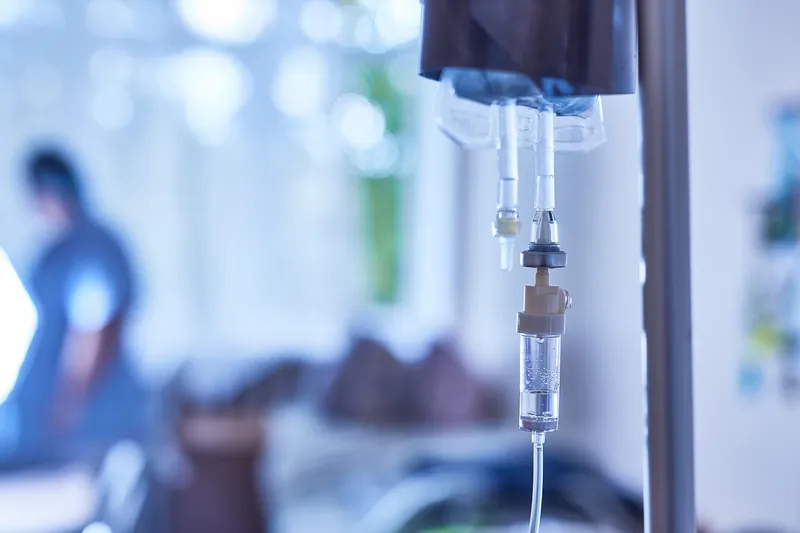 IV drip chamber and tubing hanging from a pole in a softly lit treatment room
