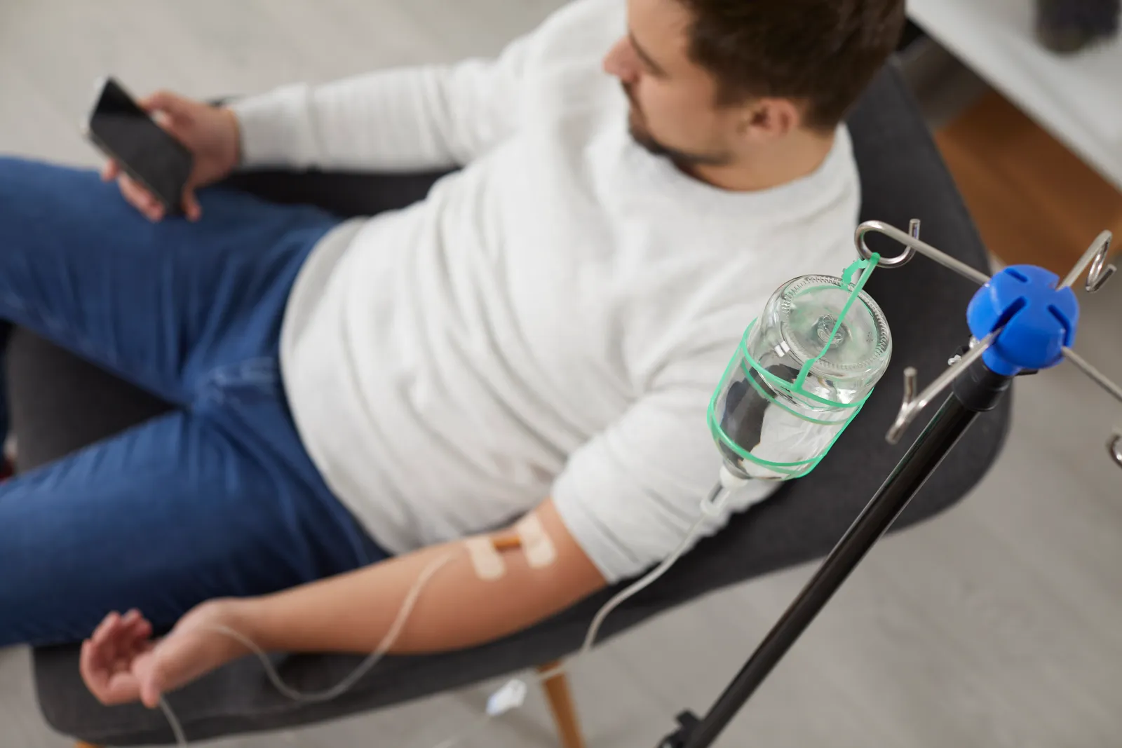 Man relaxing in a chair with a phone while receiving an IV drip in his arm