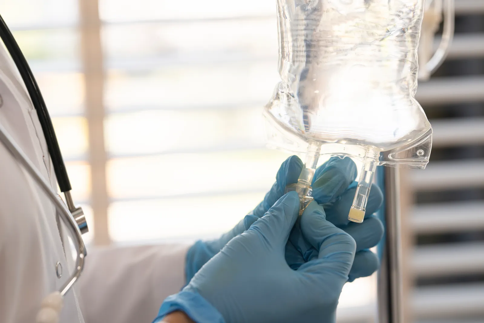 Gloved hands connect tubing to a clear IV bag