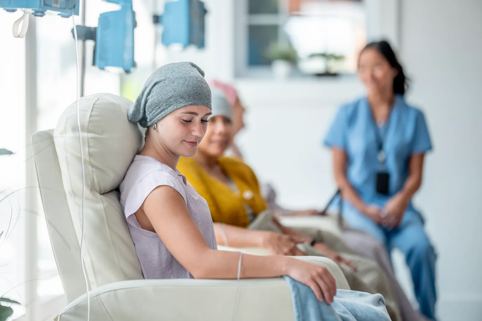 Patients wearing head coverings resting in infusion chairs while a nurse sits nearby