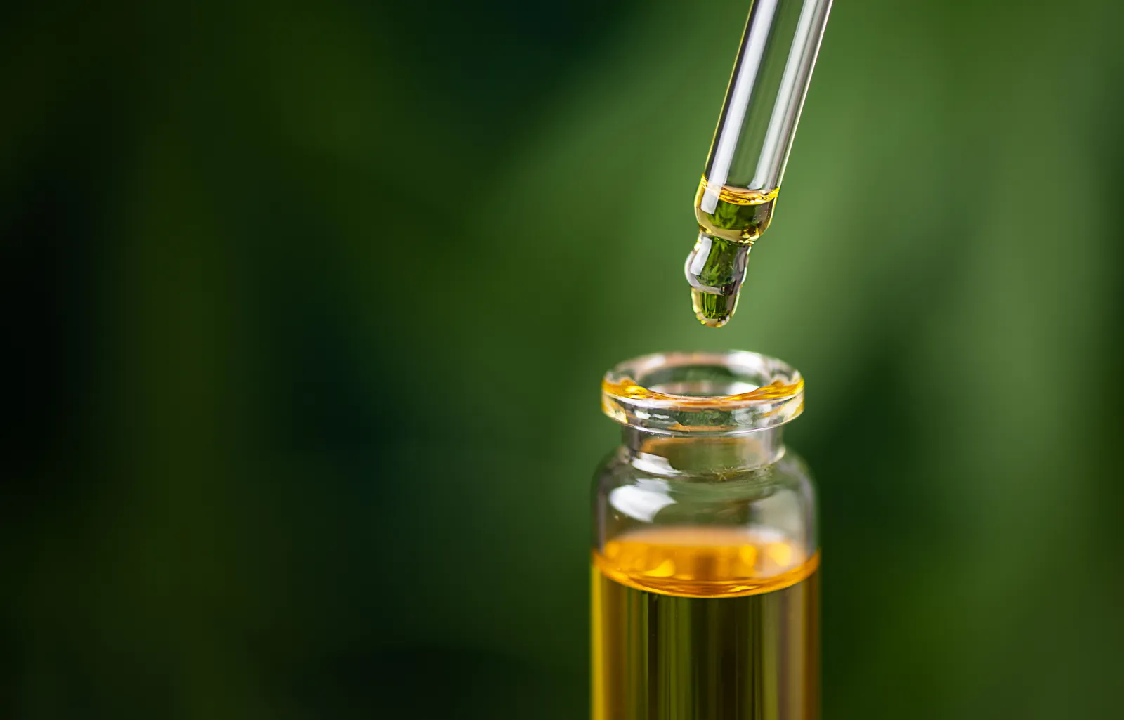 Dropper releasing golden oil into a small glass bottle against a green background