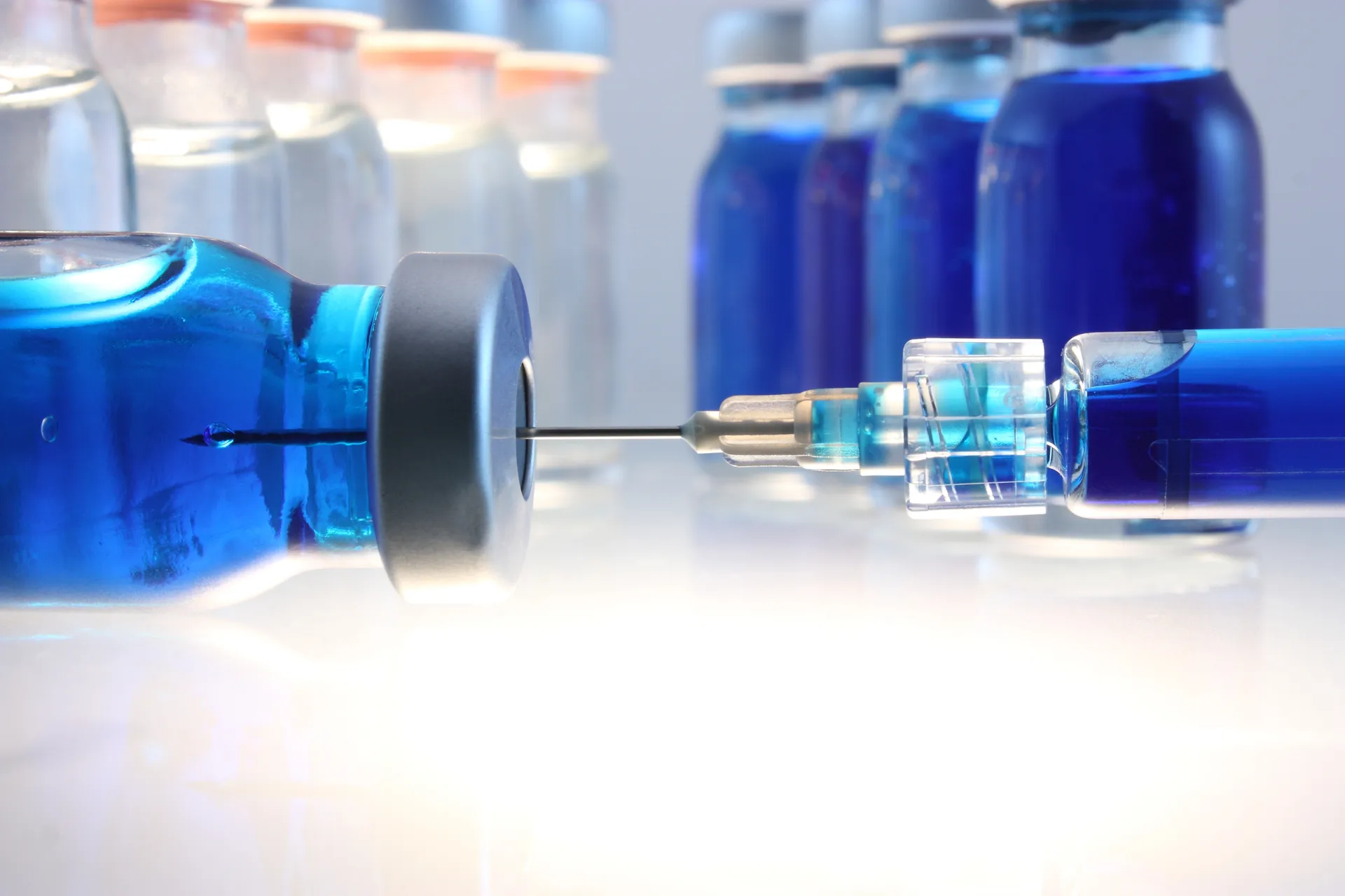 Syringe needle inserted into a vial of blue liquid with more vials in the background