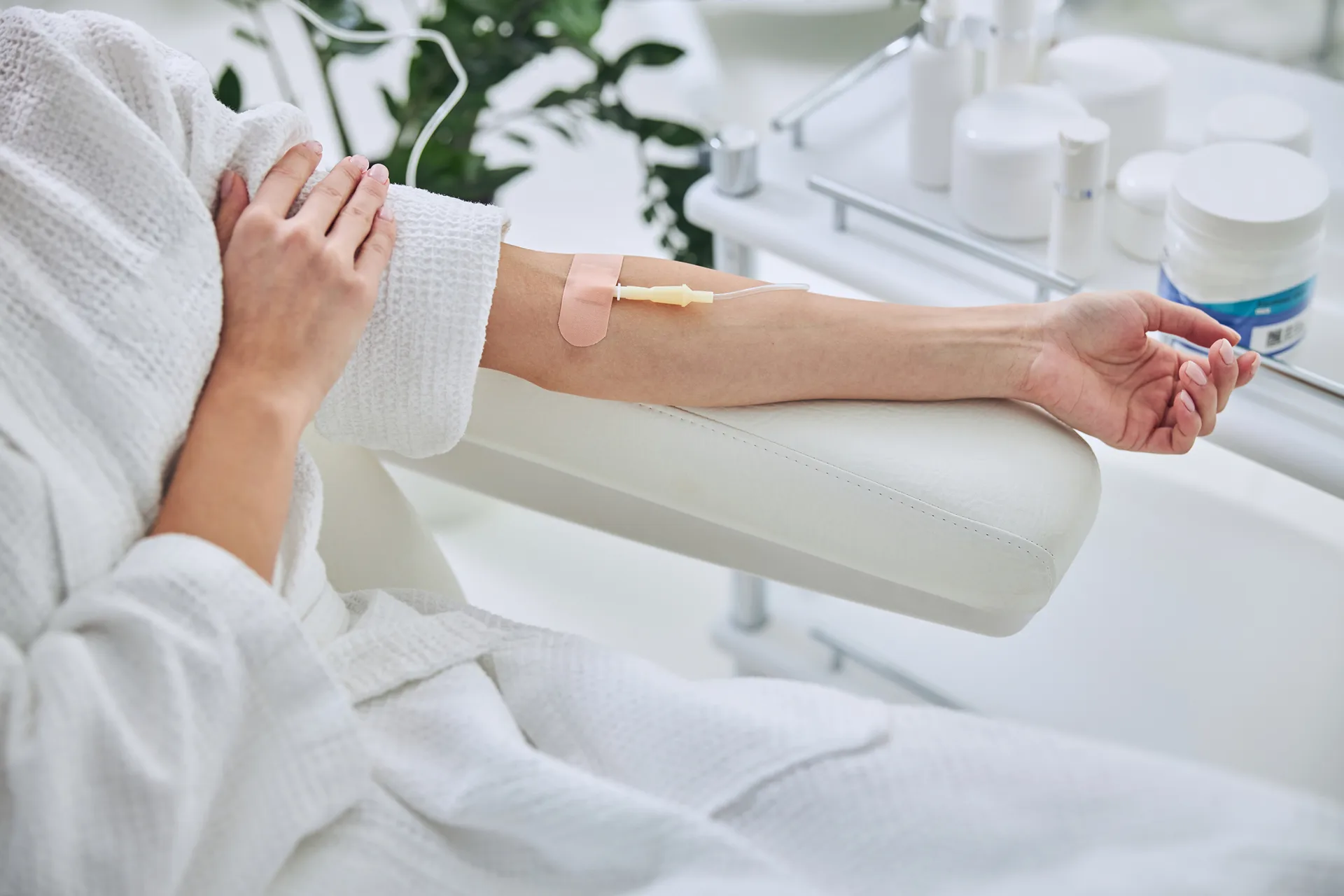 Person in a white robe rests an arm with an IV line on a white treatment chair
