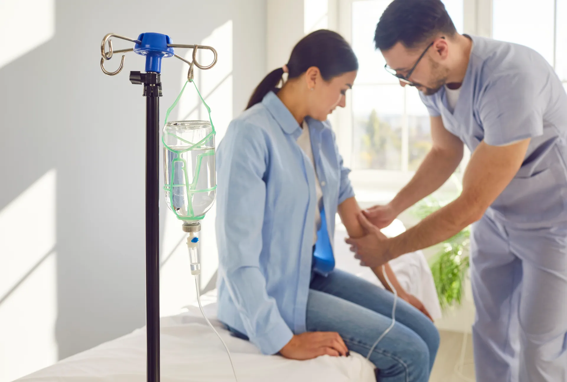 Male nurse checking a seated woman's arm beside an IV drip stand