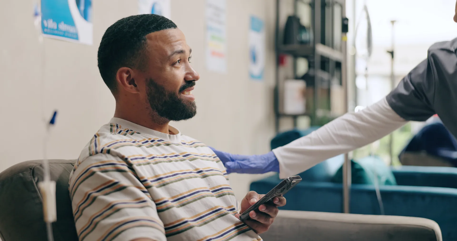 Smiling man holding a phone sits in a lounge chair as a gloved clinician reaches toward him