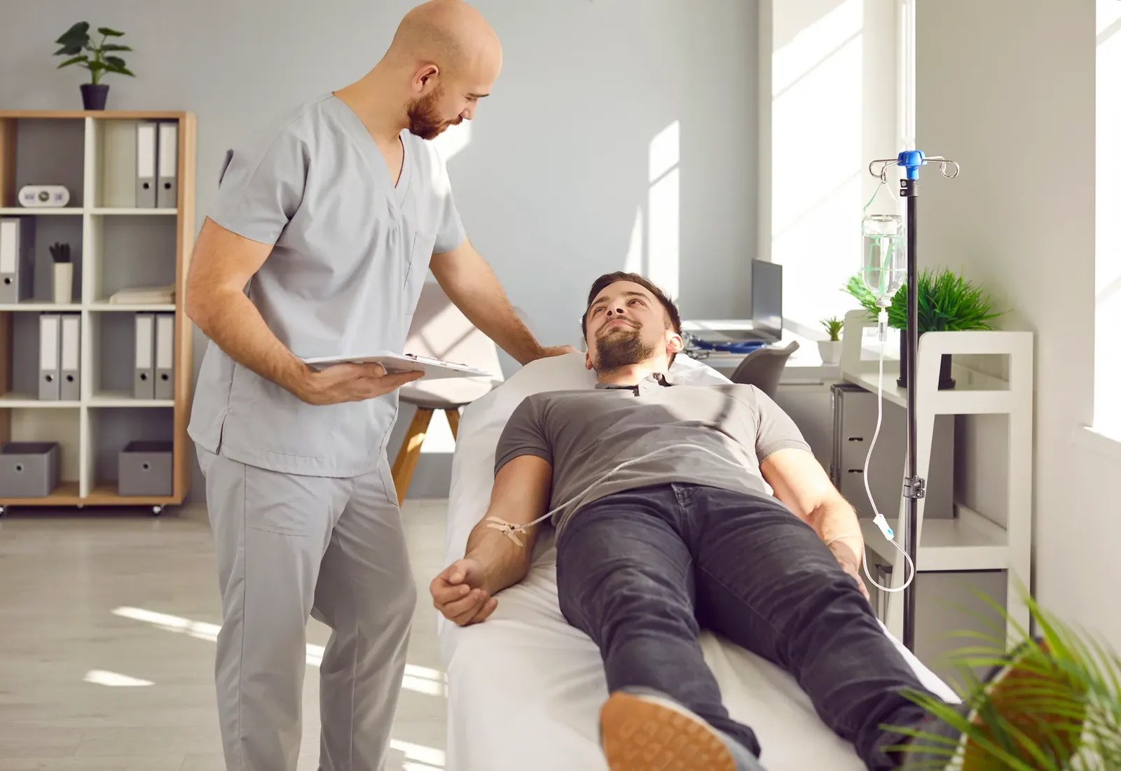 Clinician with a tablet checking on a man lying on a treatment bed with an IV line in his arm