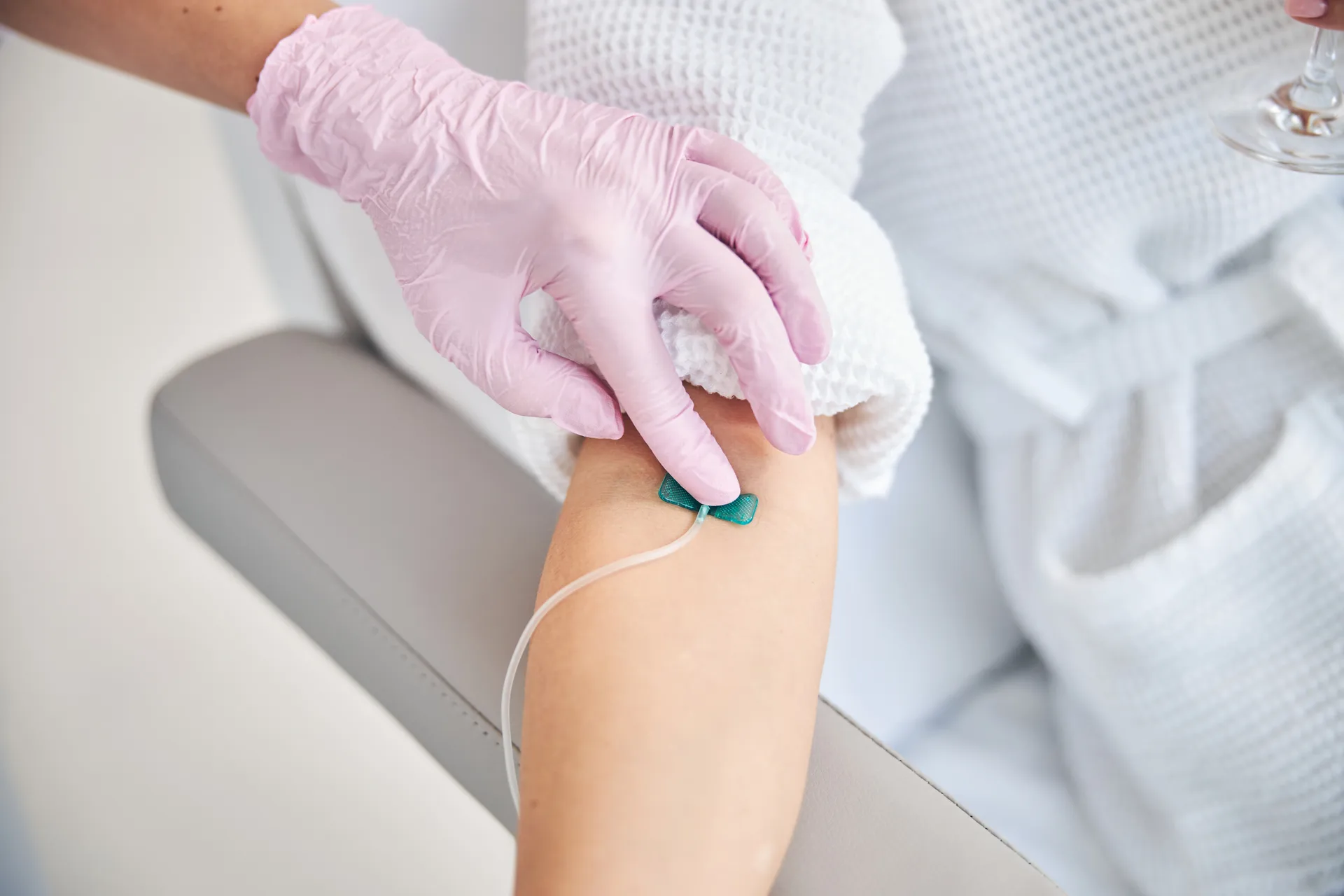 Gloved hand steadying a patient's arm with a butterfly IV needle taped in place