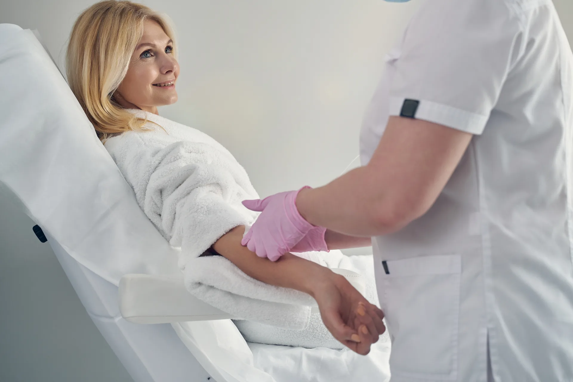Woman in a robe reclining in a treatment chair as a gloved clinician holds her arm