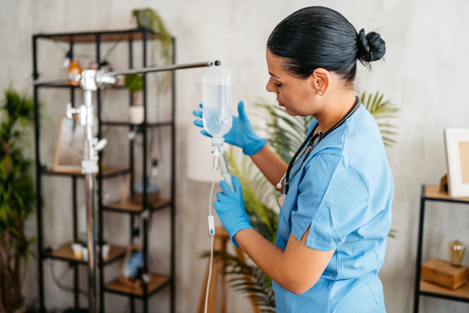 Nurse in blue scrubs and gloves adjusts an IV bag on a stand