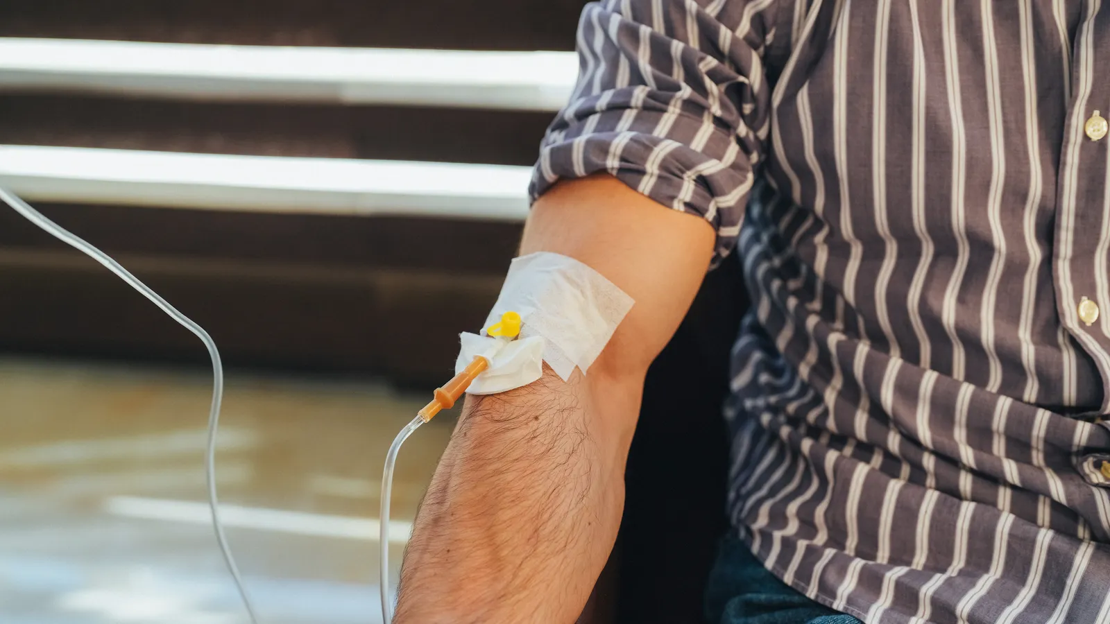 Man in a striped shirt with an IV line taped to his forearm